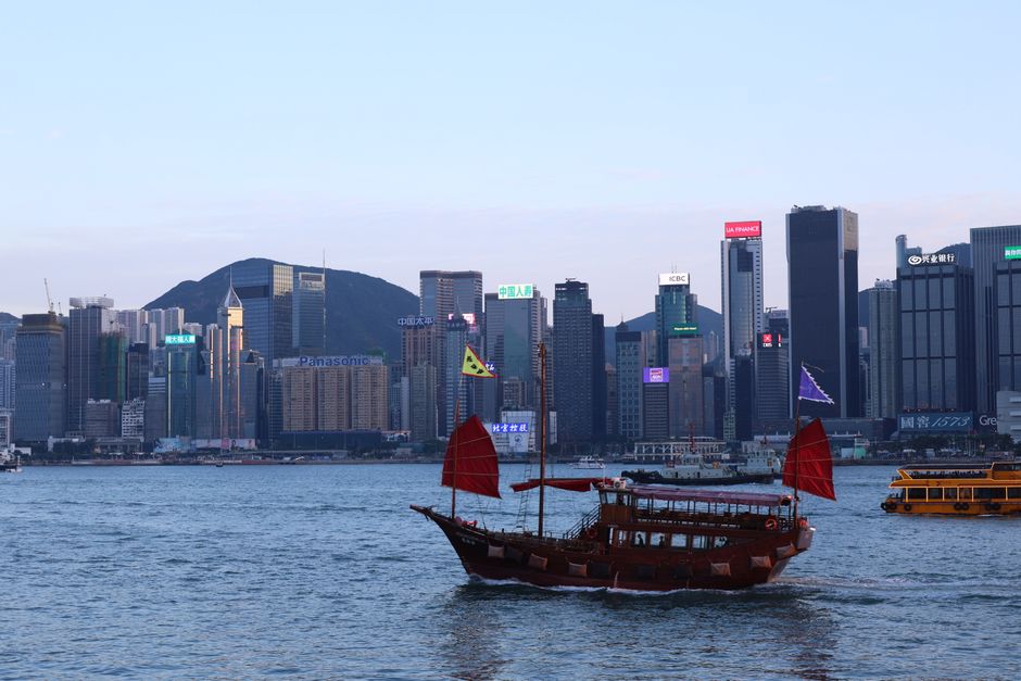 A picturesque view of a traditional junk boat sailing past Hong Kong's modern skyline at dusk.