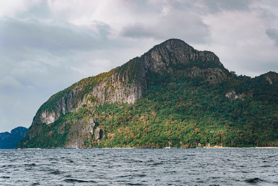 Stunning mountain island with lush greenery viewed from the sea under cloudy skies.