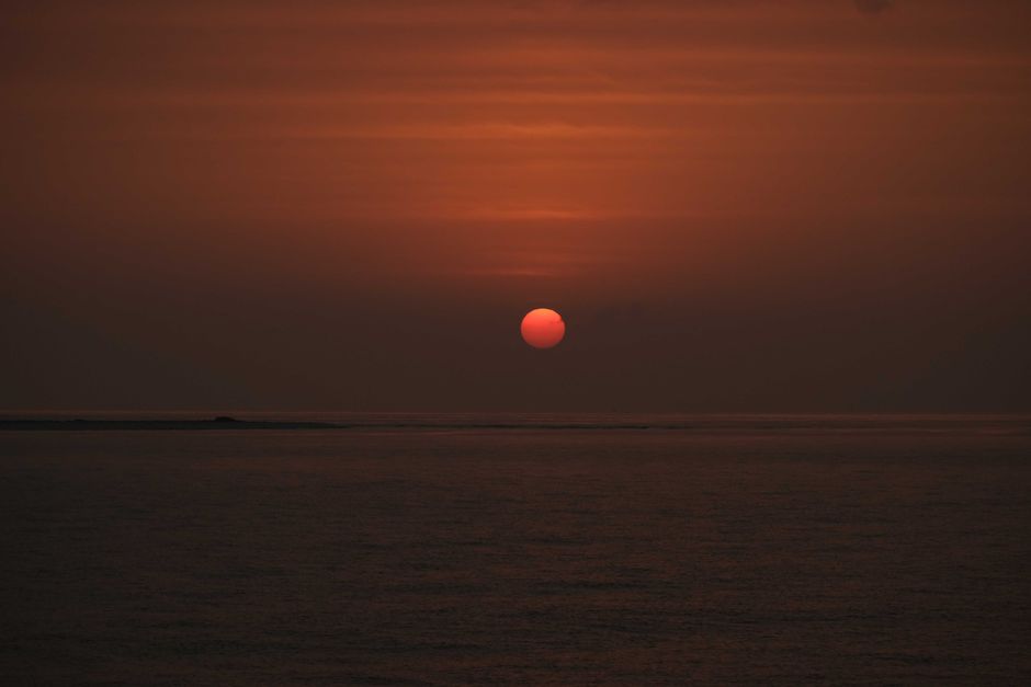 A calm ocean scene at sunset with vivid orange and red sky reflecting on water.