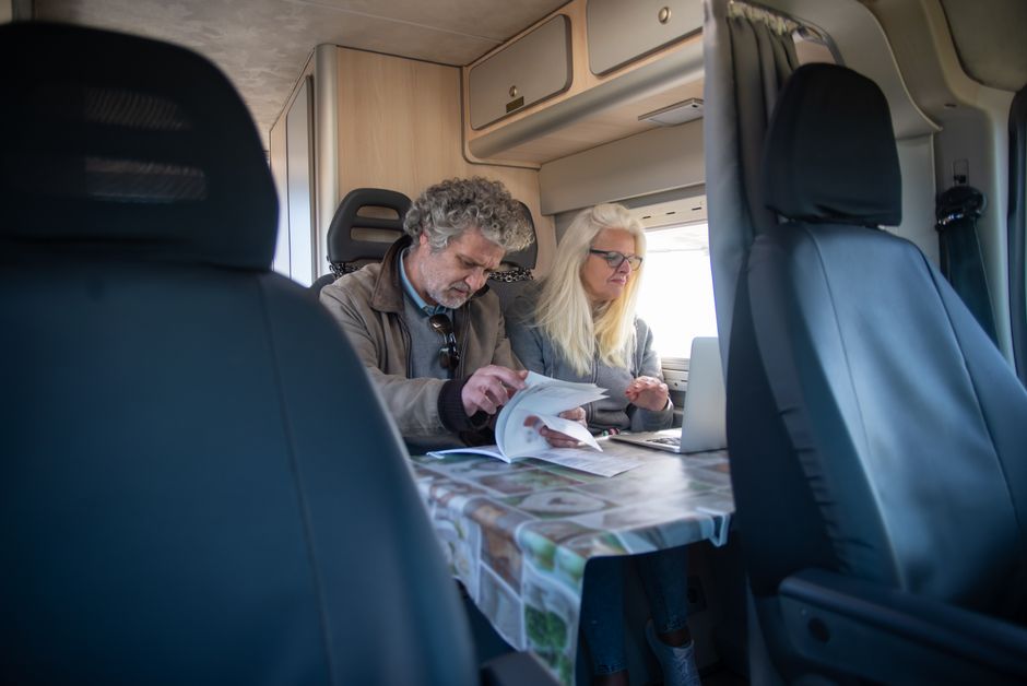 An adult couple working indoors in a caravan, using a laptop and reviewing documents.