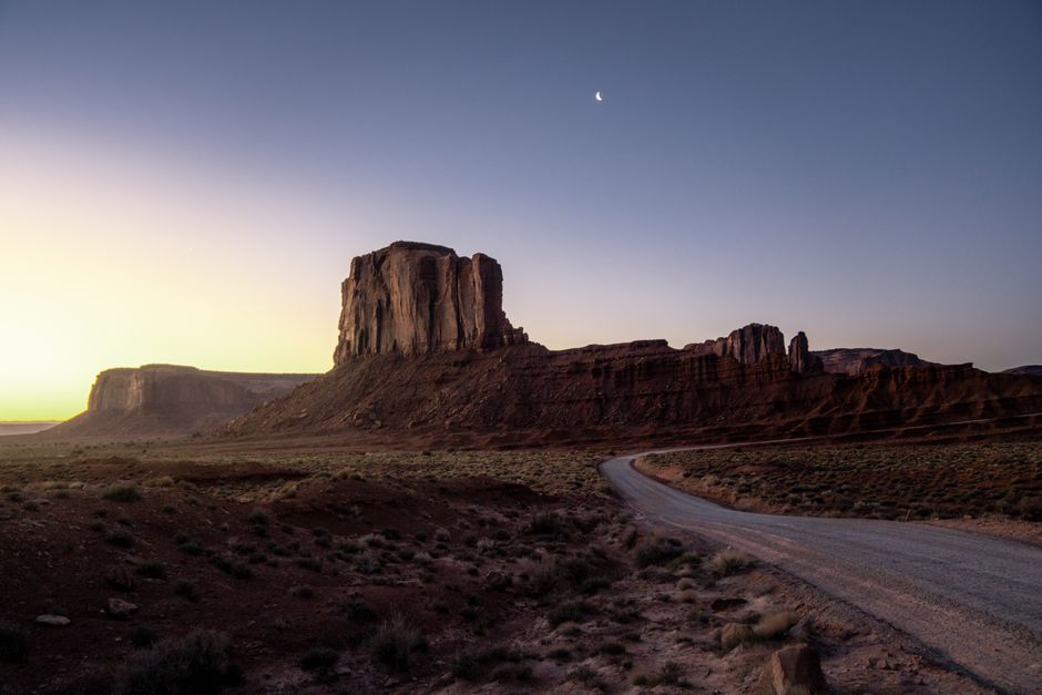 Stunning landscape of Monument Valley during twilight with visible crescent moon.