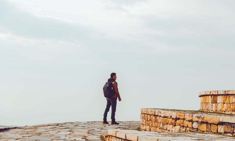 A man with a backpack walks on a stone path under a cloudy sky, symbolizing travel and exploration.