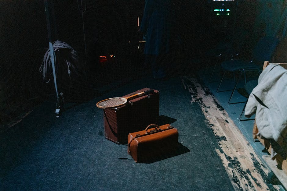 Old-fashioned suitcases with a tennis racket in a moody, dimly lit room, evoking nostalgia.