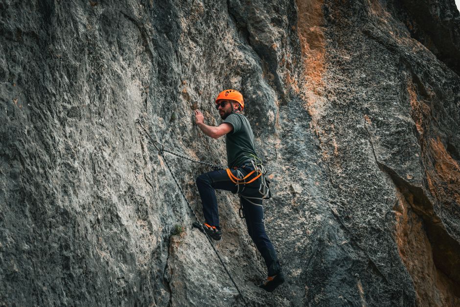 Adult male climber navigating a steep rock face with safety gear and helmet outdoors.