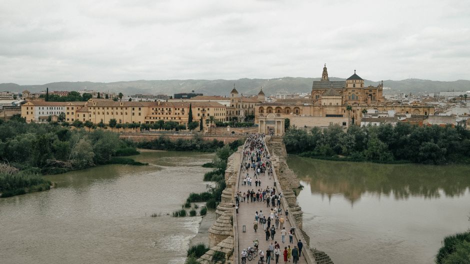 Tourists cross the historic Roman bridge in Córdoba with the Mezquita in the background.