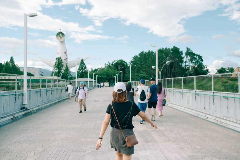 Woman in black t-shirt walking on bridge near Tower of the Sun.