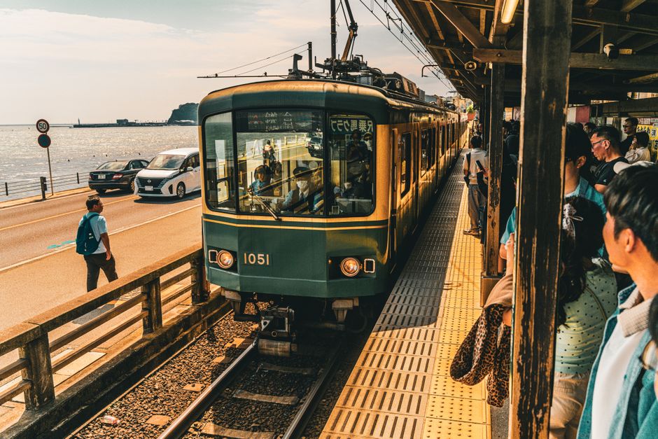 A train arrives at a busy Japanese coastal station with people waiting, highlighting travel in Japan.