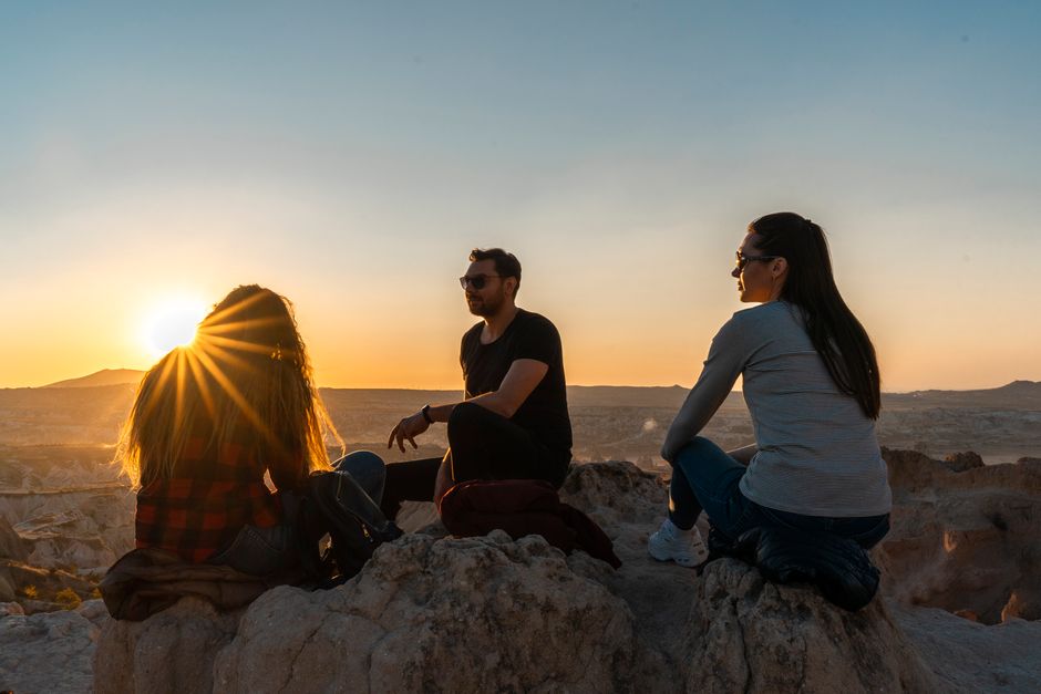 Three friends sitting on rocks, enjoying the sunset in a scenic location.