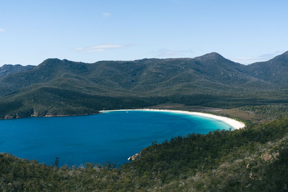 A breathtaking aerial view of Wineglass Bay's turquoise waters and lush surrounding mountains in Tasmania.