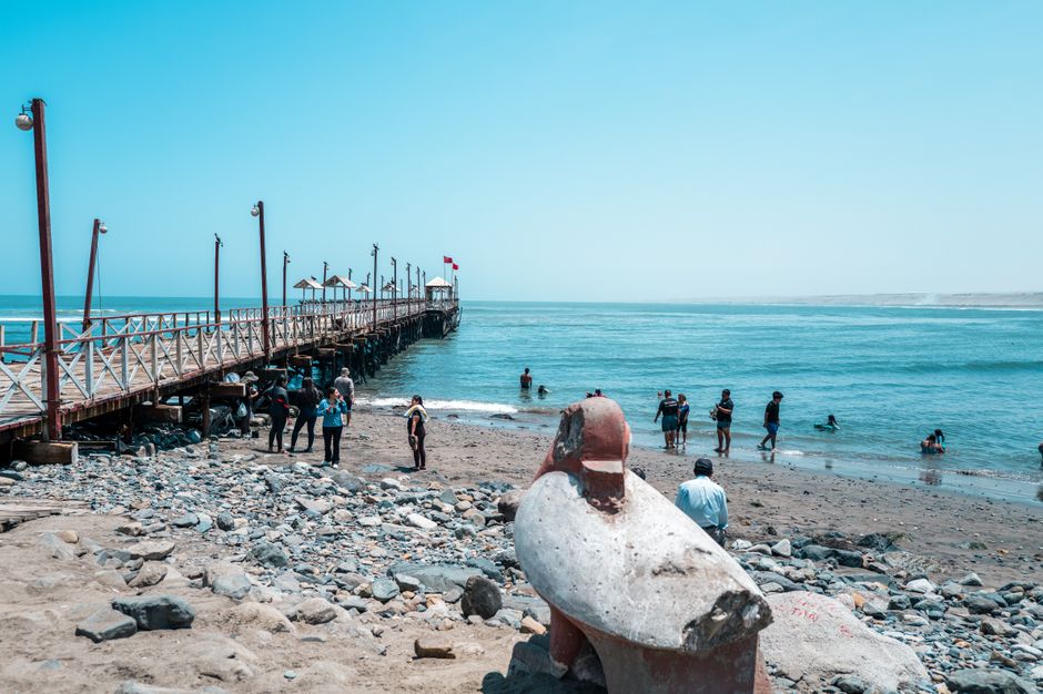 People enjoying a sunny day at Huanchaco Beach with the iconic pier in view.